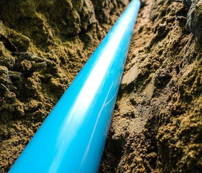 a bright blue pvc pipe being placed in dirt 