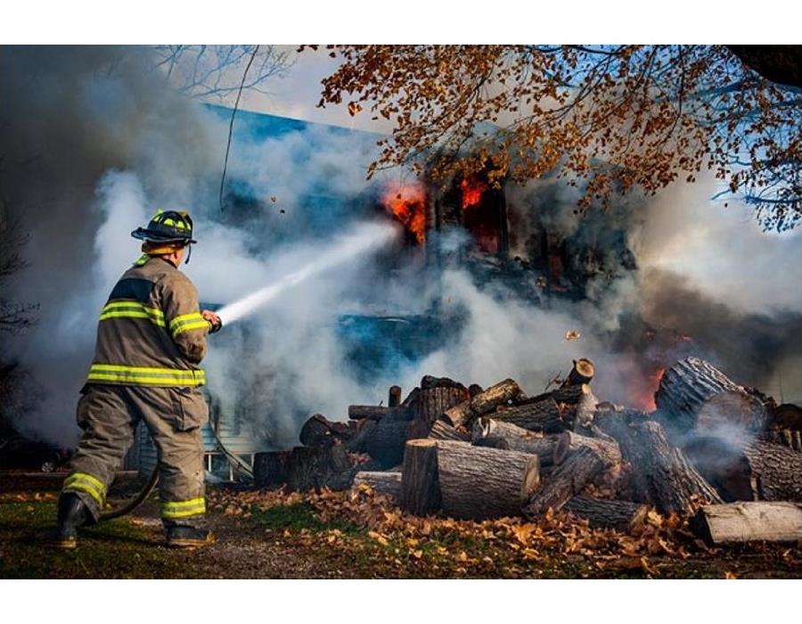 a firefighter spraying water on a large house fire